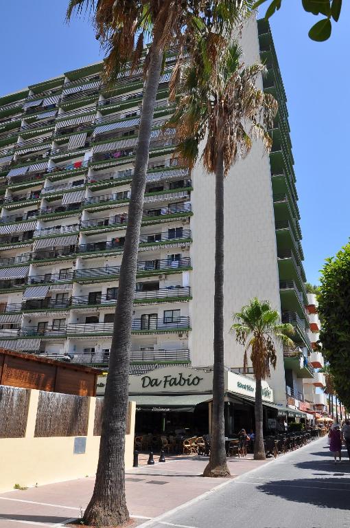 Mūsdienīgs daudzstāvu nams ar terasēm un palmu stādījumiem priekšā, blakus kafejnīca "Da Fabio". Skats uz ielu ar gājēju celiņu un kafejnīcu.