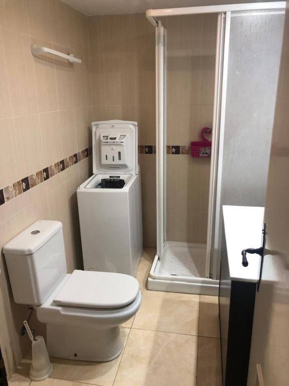 Mūsdienīgs vannas istabas interjers ar dušu, veļas mašīnu un tualeti, kas nodrošina funkcionalitāti un komfortu. Sienas ir apšūtas ar keramikas flīzēm.