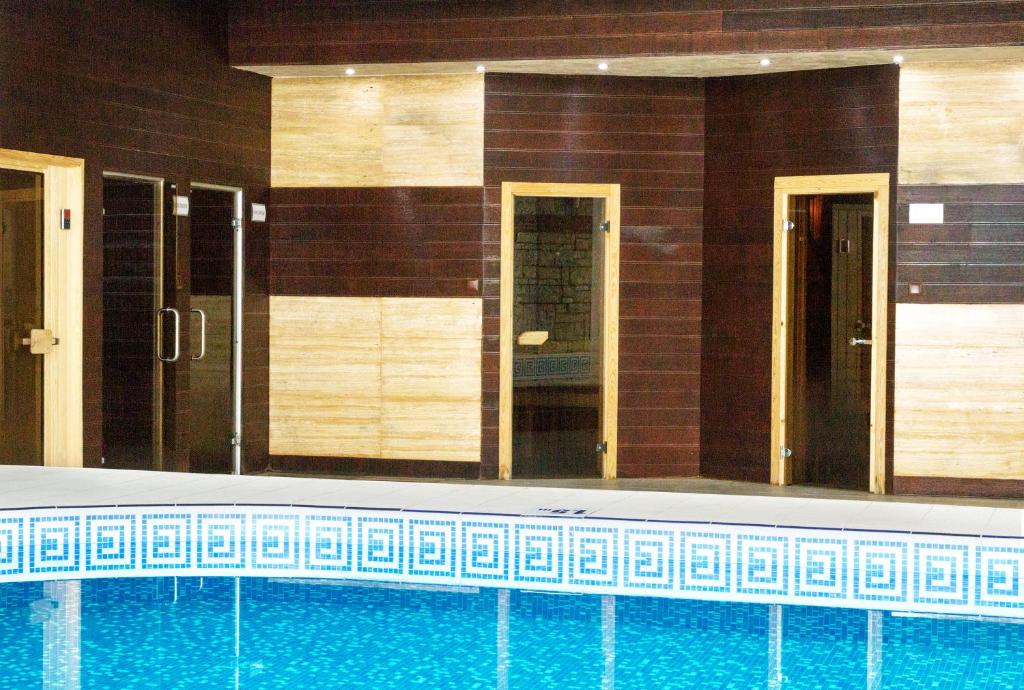 Mūsdienīgs peldbaseins ar koka apdari un vairākiem ieejas durvīm uz saunām, radot relaksējošu atmosfēru.