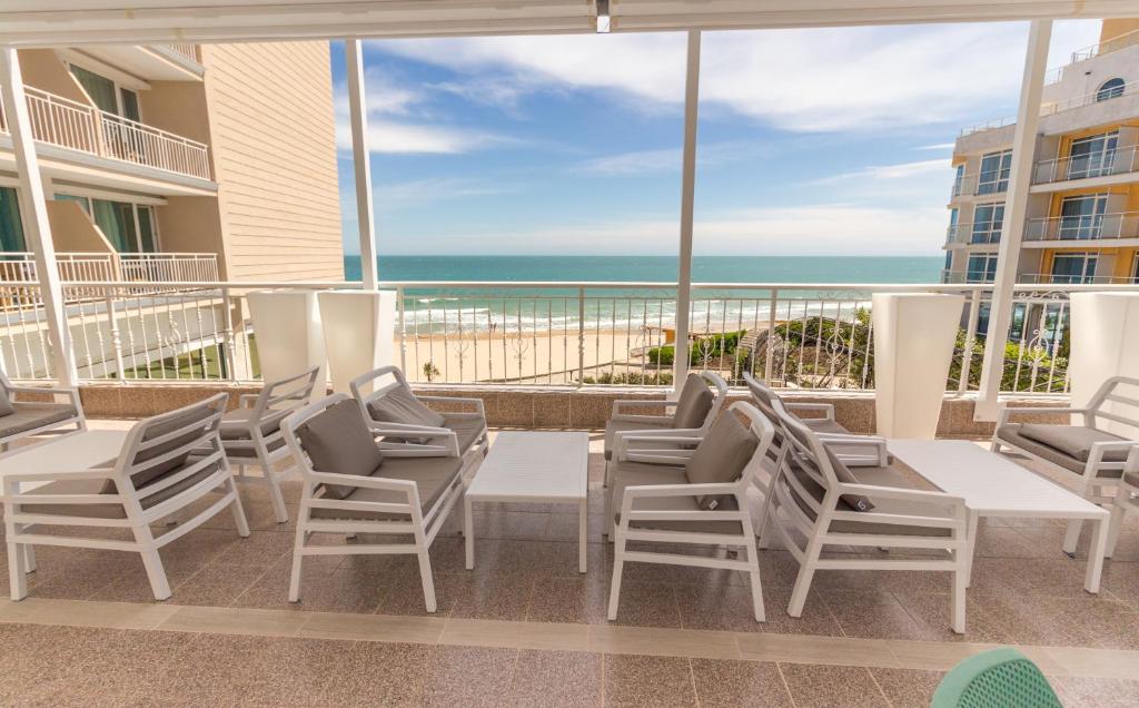 Terases skats uz pludmali un jūru, kur baltas mēbeles nodrošina ērtu atpūtu. Gaisma ieplūst caur plašajiem logiem, radot relaksējošu atmosfēru.