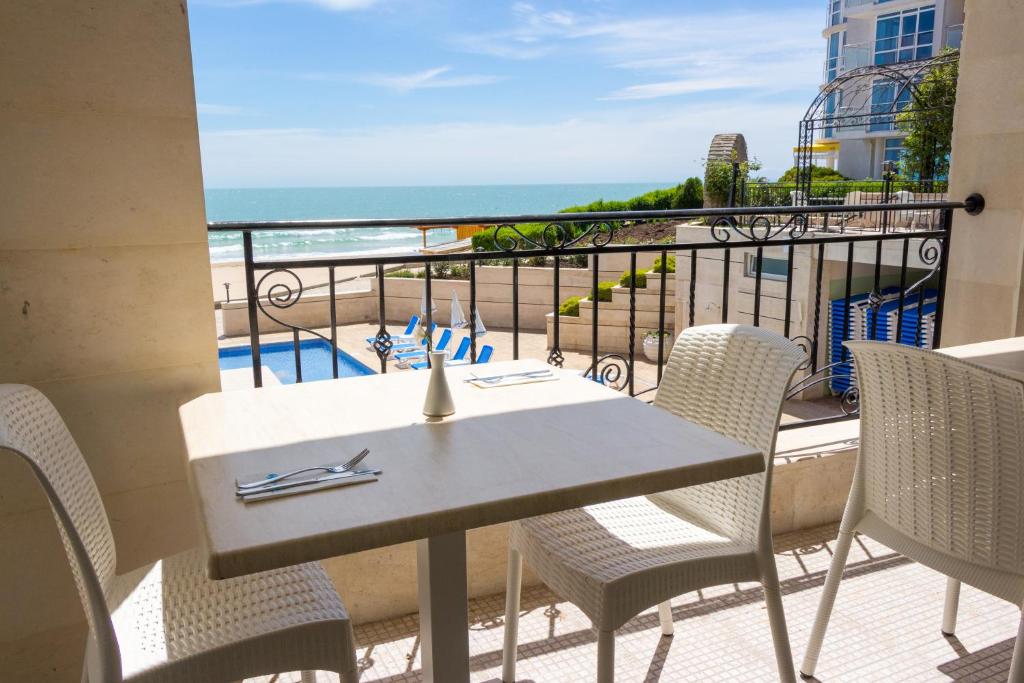 Balcony view of a seaside restaurant with a table set for dining, overlooking the beach and ocean. Sunlight illuminates the area, enhancing the inviting atmosphere.