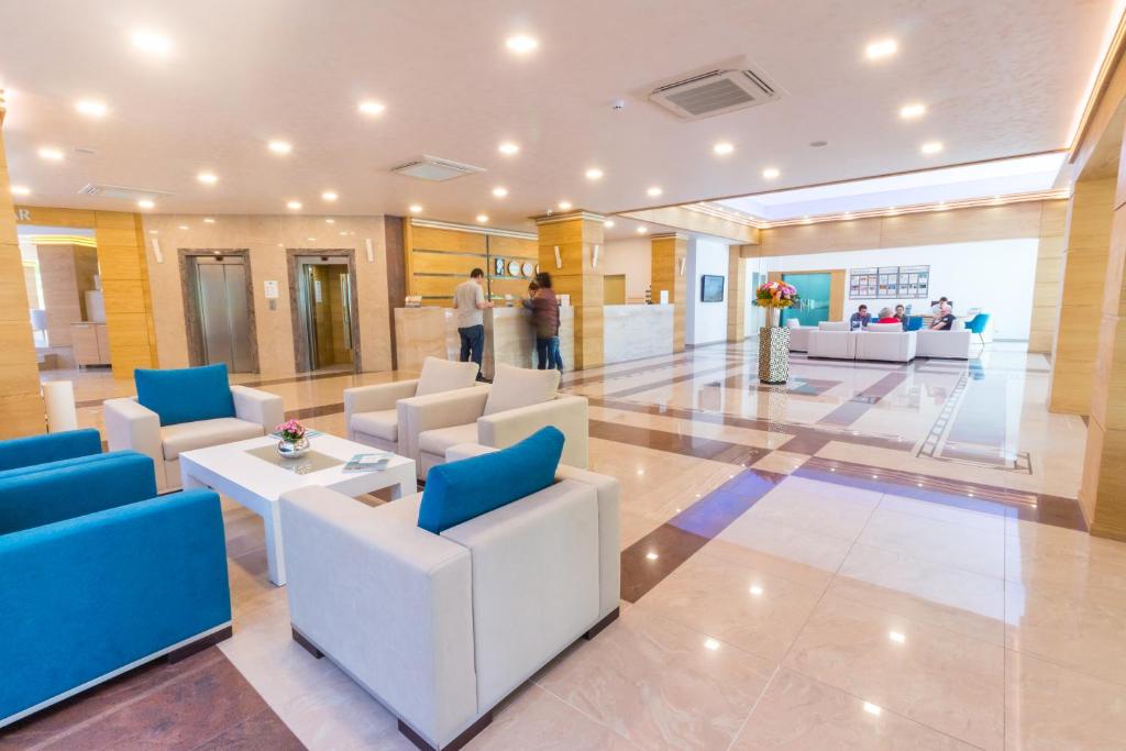 Moderns viesnīcas reģistratūras interjers ar ērtām mēbelēm un gaišu apgaismojumu. Redzami apmeklētāji, kas veic reģistrāciju pie letes.