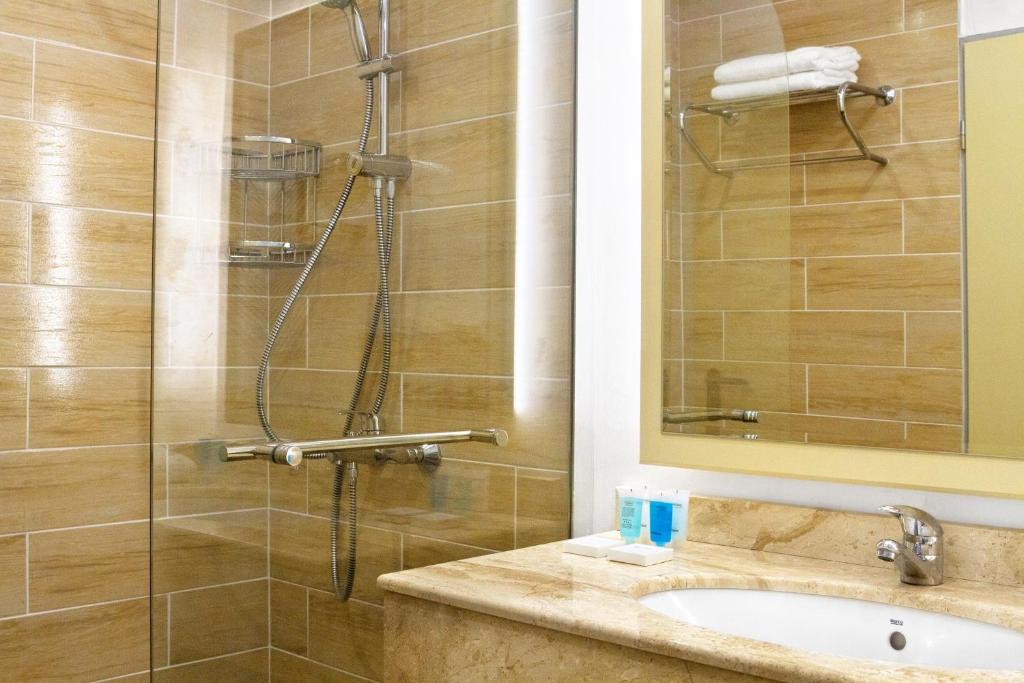 Mūsdienīgs vannas istabas interjers ar stikla dušas kabīni un elegantu akmens izskata izlietni. Rūpīgi sakārtoti higiēnas līdzekļi un dvieļi, radot patīkamu un sakārtotu atmosfēru.