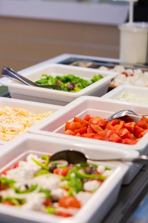 Svaigu dārzeņu uzkodu bārs ar vairākiem salātu sastāvdaļām, tostarp tomātiem, zaļajiem salātiem un sieru, pasniegts baltās bļodās.