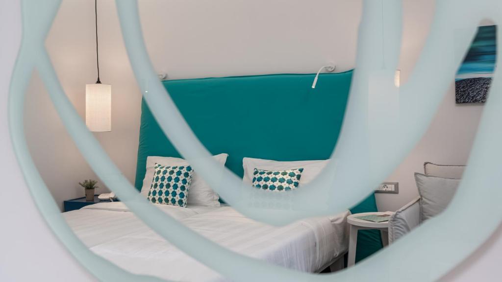 Mūsdienīgs viesnīcas numurs ar teal krāsas akcentiem un elegantu apgaismojumu. Skats caur dekoratīvu stikla elementu uz gultu un interjeru.