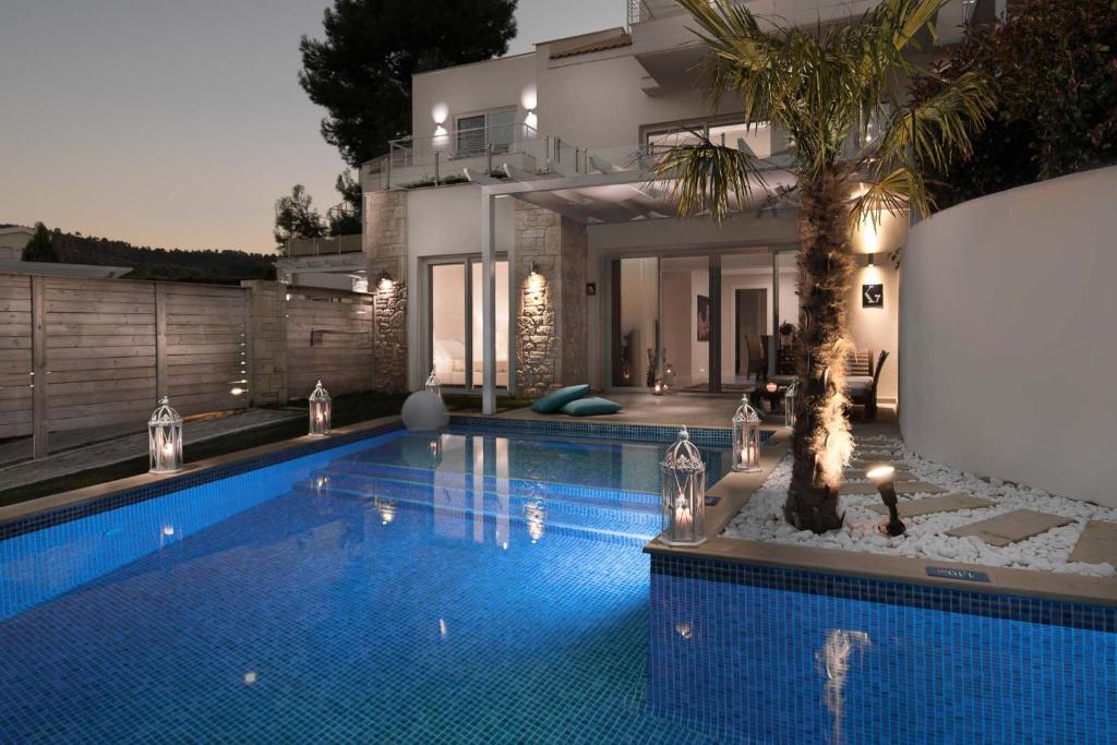 Mūsdienīga māja ar baseinu, apgaismojumu un palmām, kas rada relaksējošu atmosfēru. Baseina ūdens spīd starp nakts gaismu, radot elegantu un mierīgu vidi.