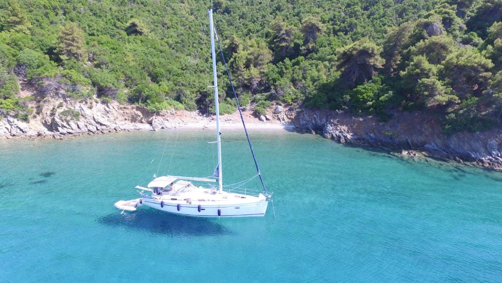 Jahts peldošs kristāldzidros ūdeņos, apkārt izteikta zaļā auga ainava. Mierīga pludmale un klusa atmosfēra.