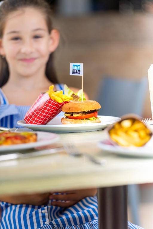 Bērns ar ēdienu SeaLife Family Resort Hotel, burgeris un frī kartupeļi uz galda.