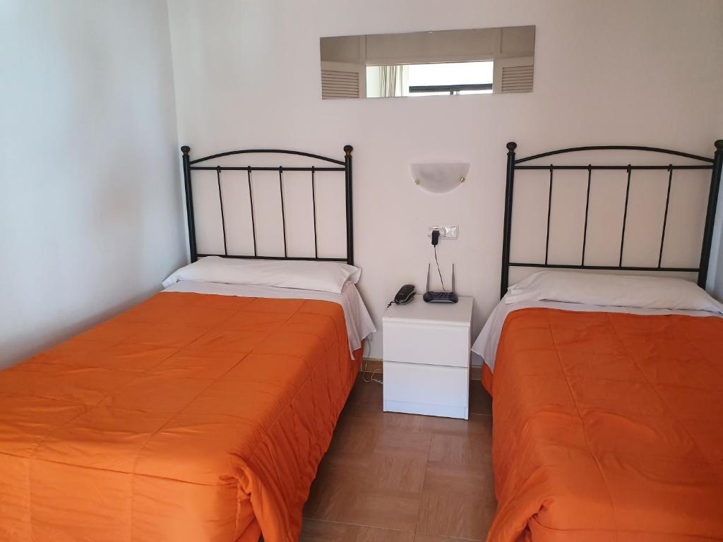 Divvietīga guļamistaba ar divām atsevišķām gultām, oranžām segām un baltiem gultas veļas komplektiem. Telpā ir vienkāršs naktsgaldiņš un spogulis.