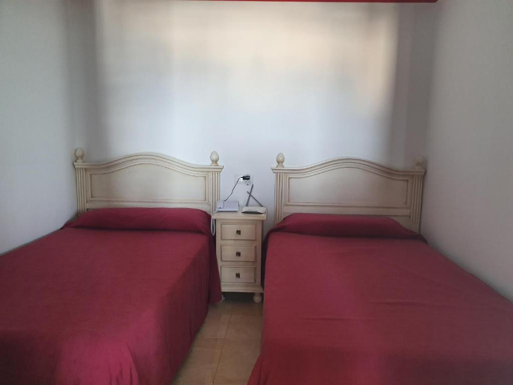 Divas gultas ar sarkanām gultas veļām un blakus esoša nakts skapīša ar lampu. Telpa ir gaiša un vienkārša, radot mājīgu atmosfēru.