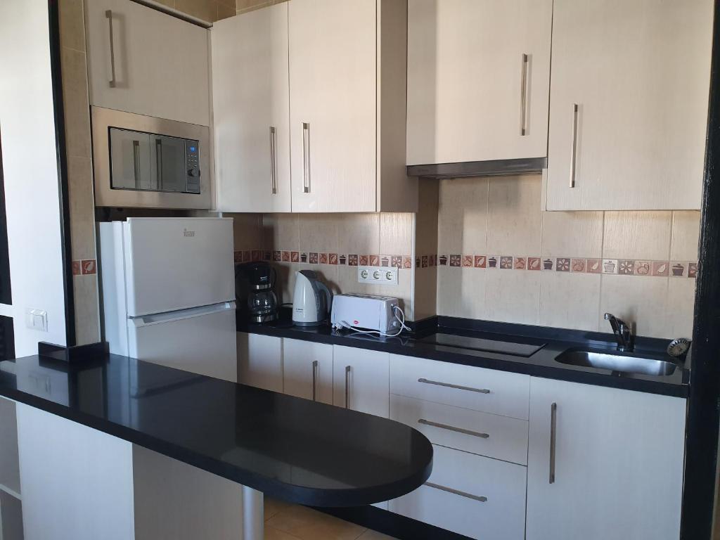 Mūsdienīga virtuve ar gaišām skapīšu frontēm, melnu darba virsmu un iekārtām, tostarp ledusskapi, mikroviņu un kafijas automātu. Virtuve ir funkcionāla un labi aprīkota.