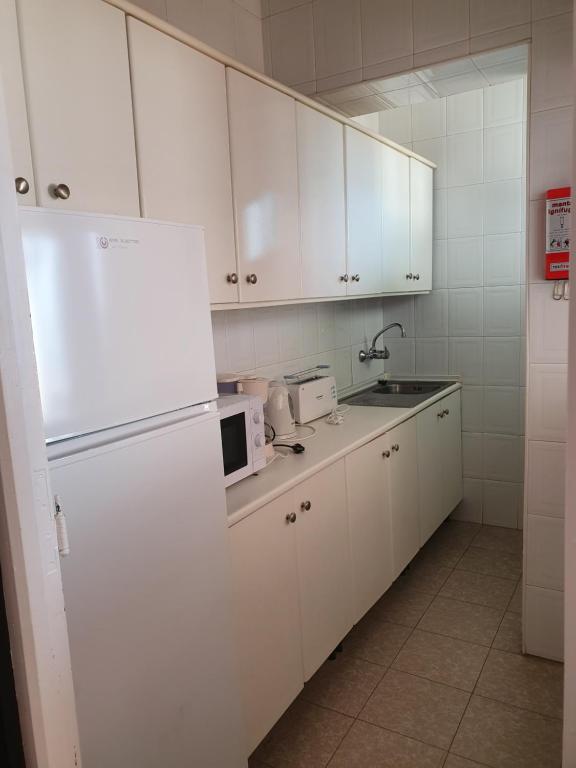 Gaiša virtuve ar baltām skapītēm, ledusskapi, mikroviļņu krāsni un izlietni, piedāvā ērtu un sakārtotu telpu ikdienas lietošanai.