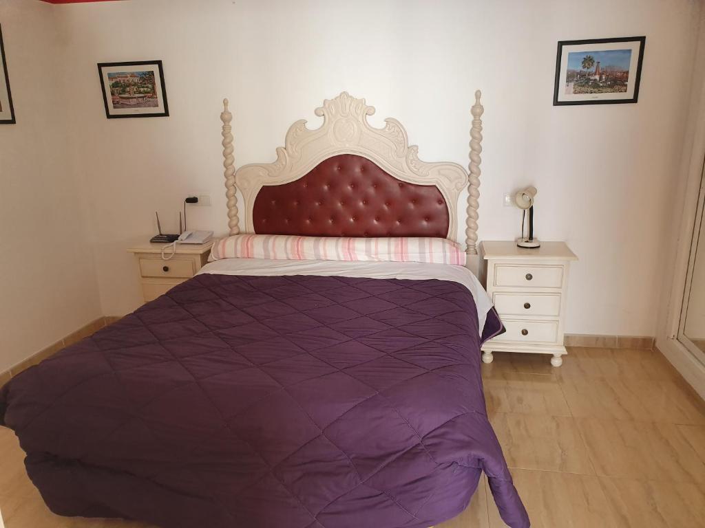 Guļamistaba ar lielu gultu ar izstrādātu galvgali, pārklātu ar violetu segu. Telpā atrodas naktsgaldiņš un lampa, kā arī dekoratīvi attēli pie sienas.