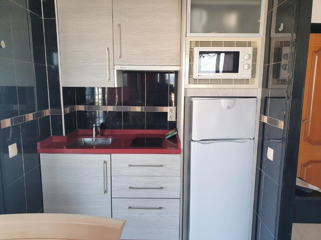 Mūsdienīga virtuve ar sarkanu darba virsmu, ledusskapi un mikroviļņu krāsni, kas iekārtota melna un pelēka toņu kombinācijā. Virtuve ir kompaktā izmērā, piemērota mazām telpām.