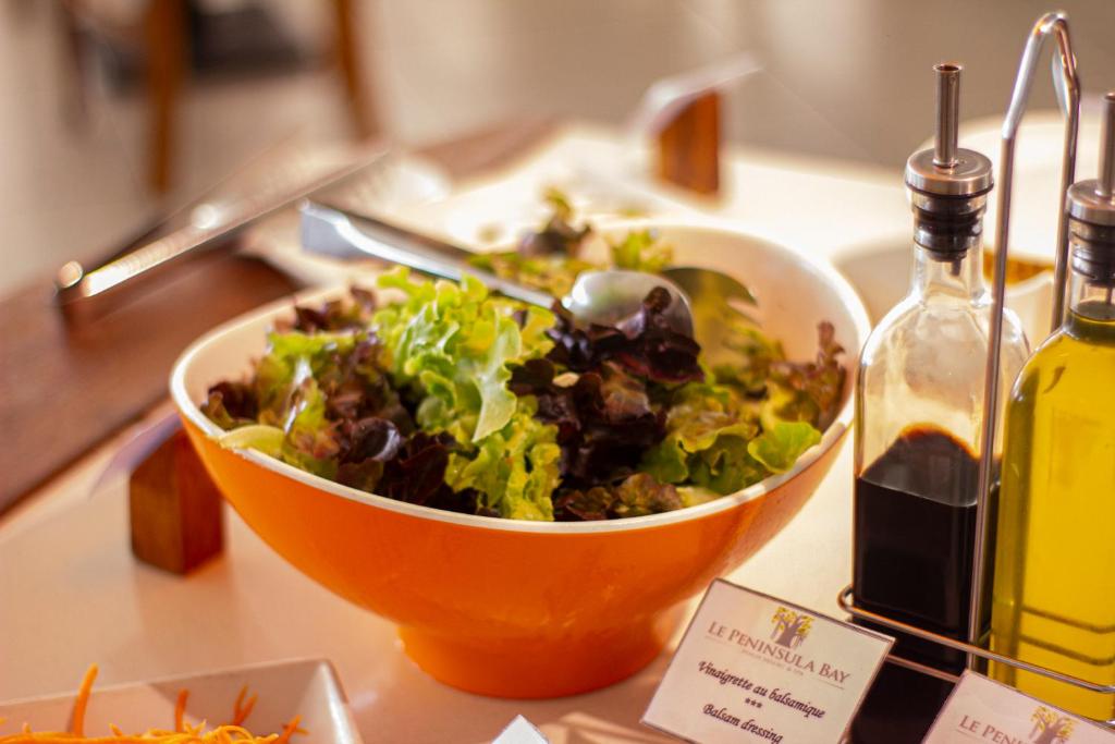 Svaigu salātu bļoda ar zaļumiem un mērci, pievienoti eļļas un balzamiko etiķa pudeles.