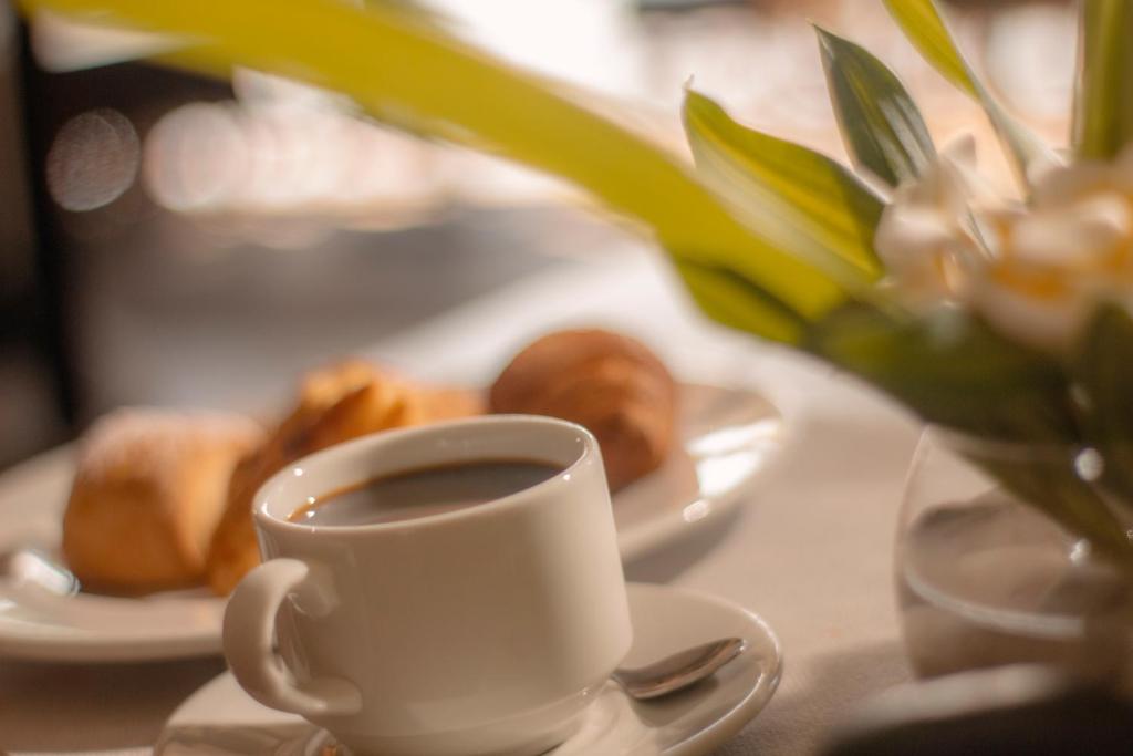 Svaigas kafijas tase ar konditorejas izstrādājumiem un ziediem, radot patīkamu brokastu atmosfēru.