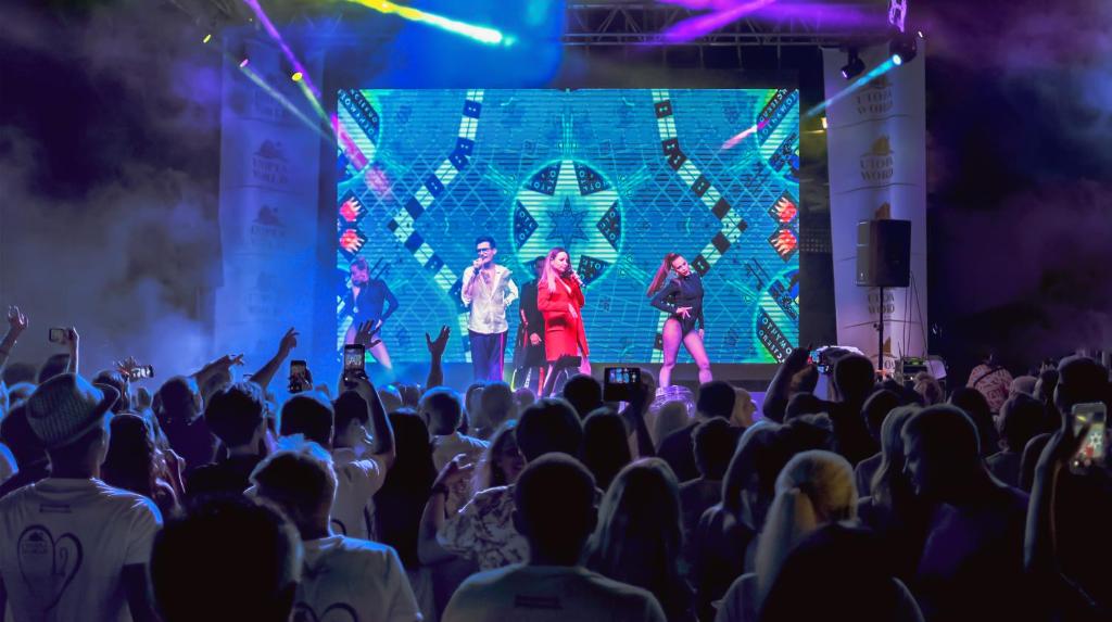 Uz skatuves izpildītāji un pūlis Utopia World Hotel muzikālajā pasākumā.