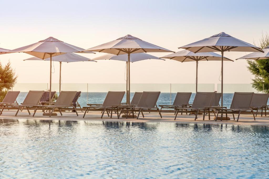 Peldbaseins ar saulessargiem un atpūtas krēsliem, kas piedāvā mierīgu atmosfēru pie jūras. Skats uz horizontu un saulrietu rada relaksējošu noskaņu.