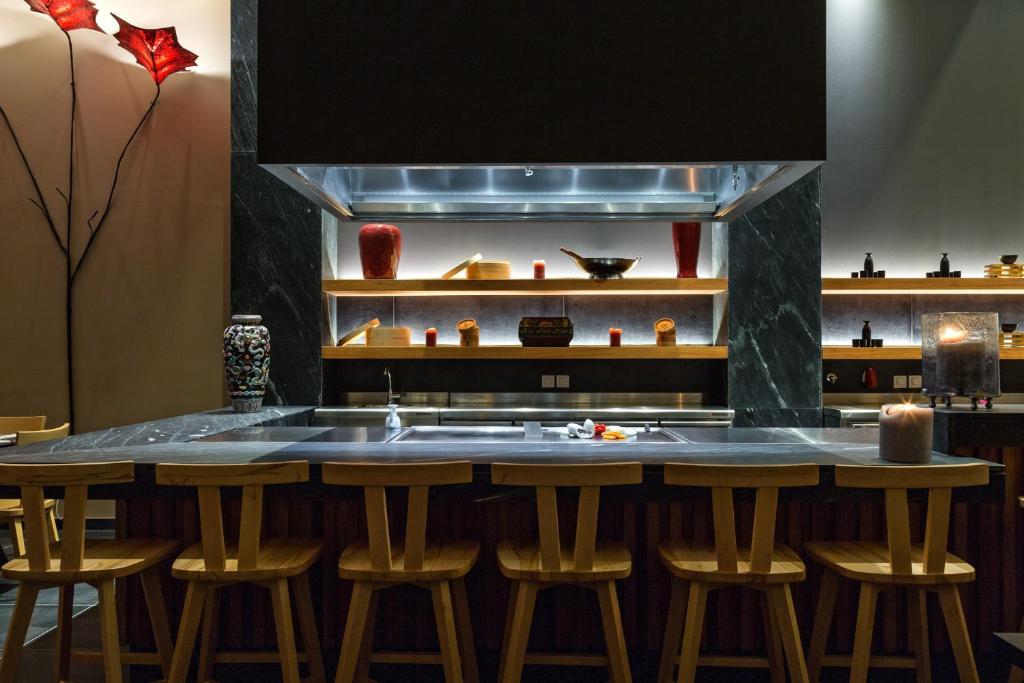 Mūsdienīga virtuves telpa ar melno marmora galdu, koka krēsliem un elegantiem dekoratīviem elementiem. Apgaismojums akcentē estētiku un rada siltu atmosfēru.