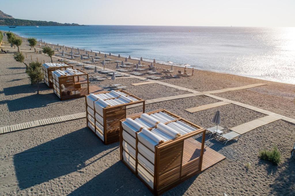 Pludmales ainava ar modernām koka kabīnēm, kas nodrošina ērtu atpūtu, blakus saulessargiem un pludmales krēsliem. Skats uz mierīgu jūru un saulainu debesi.