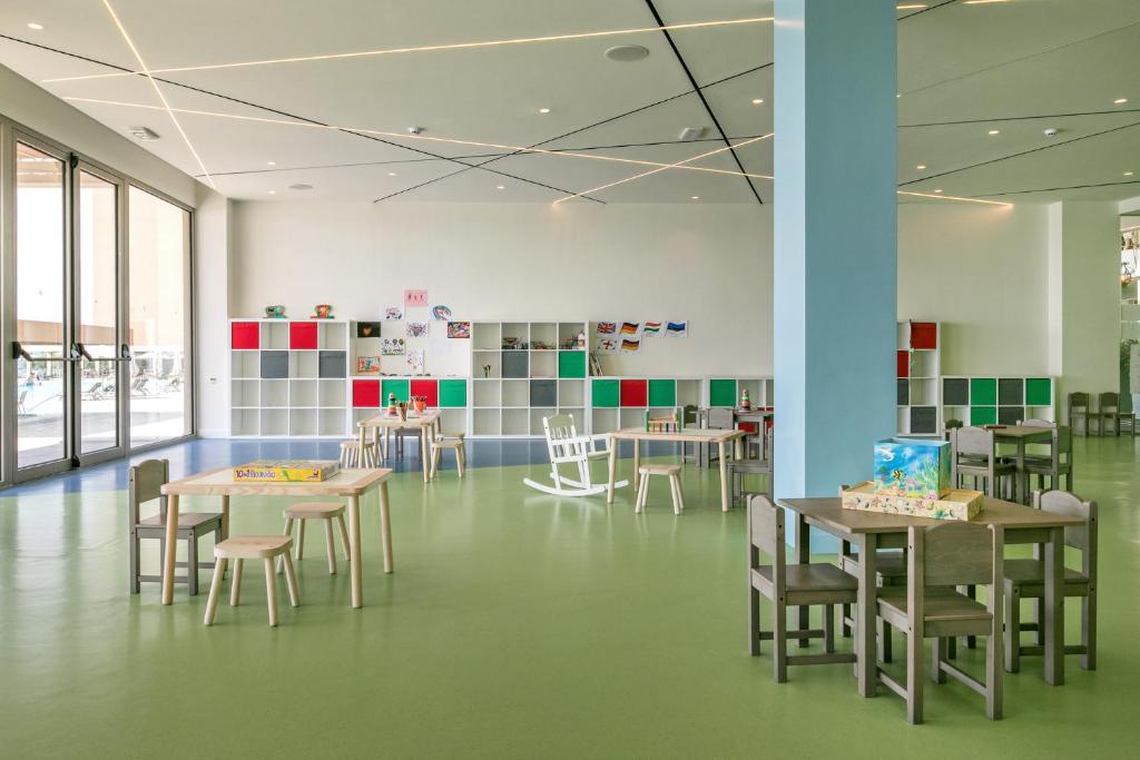 Mūsdienīgs bērnu rotaļu istabas interjers ar gaišām krāsām, koka mēbelēm un krāsainiem plauktiem. Telpa ir plaša un gaiša, piemērota radošām aktivitātēm.