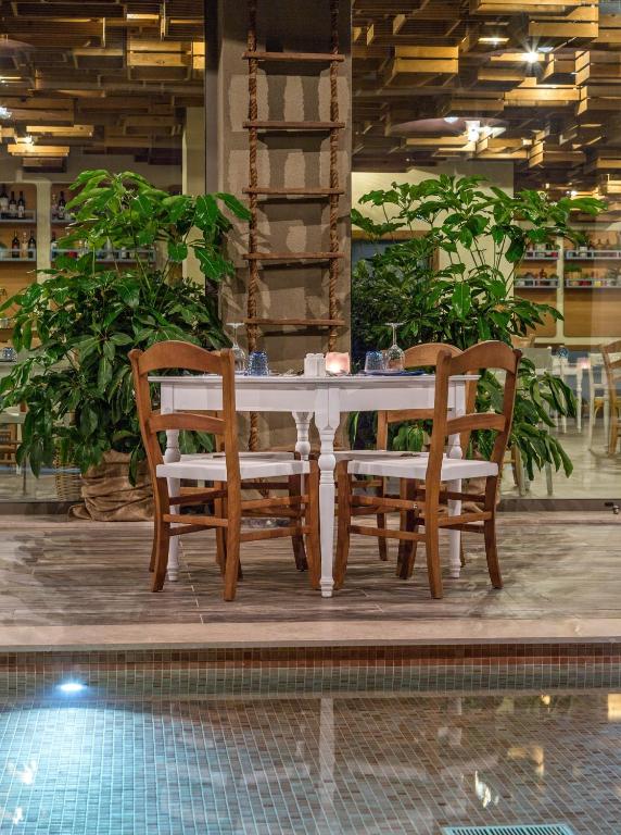 Gaismas apstākļos iekārtota romantiska ēdamzona ar baltu galdu, koka krēsliem un zaļām augu dekorācijām, kas papildina relaksējošo atmosfēru.