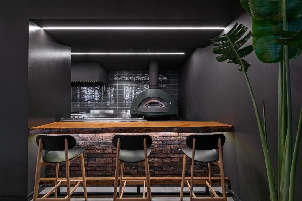 Mūsdienīga virtuve ar akmens apdari un koka bāru, kurā ir redzams malkas krāsns. Tumšas krāsas un stilīgas gaismas veido elegantu atmosfēru.