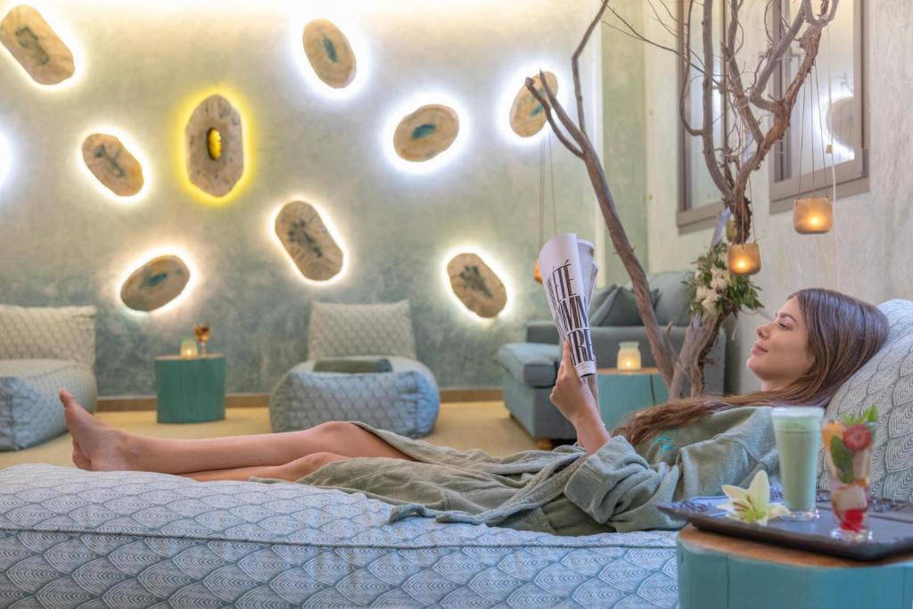 Sieviete relaksējas spa vidē, lasot žurnālu un baudot dzērienu, kamēr apkārt ir mīkstas mēbeles un dekoratīvi gaismas elementi.