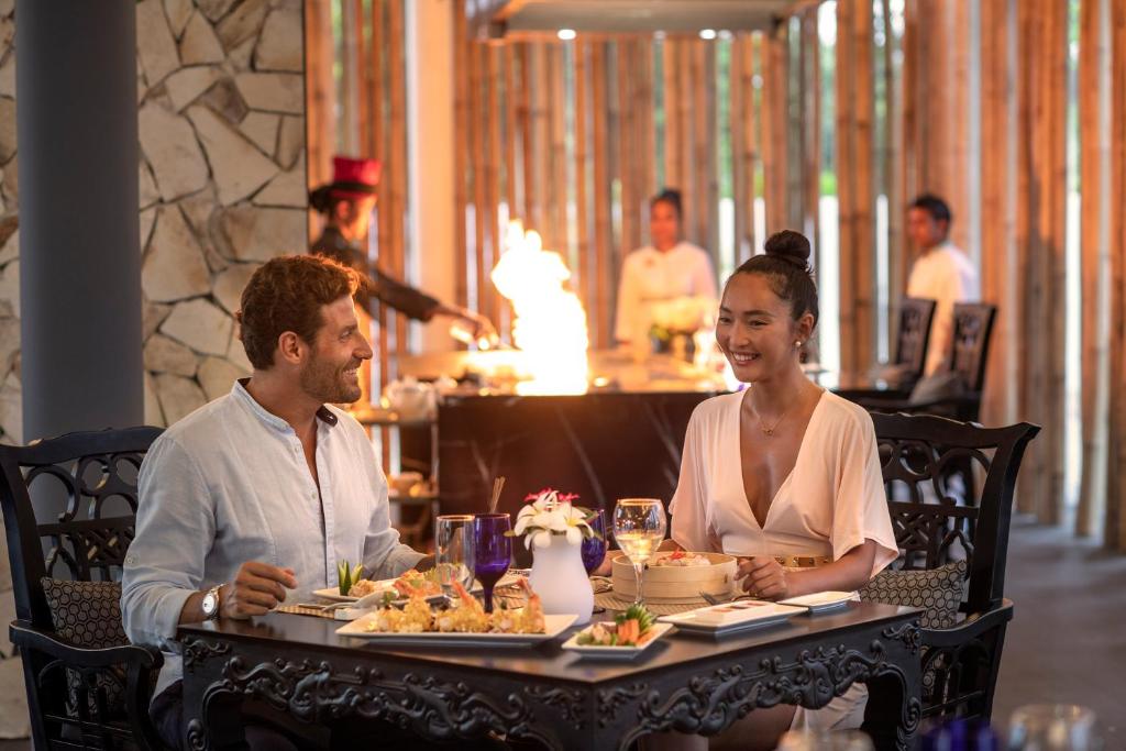 Romantiska vakariņas elegantā restorānā, kur pāris baudīja delikātus ēdienus, kamēr šefpavārs demonstrēja uguns šovu. Atmosfēra ir silta un intīma, radot patīkamu pieredzi.