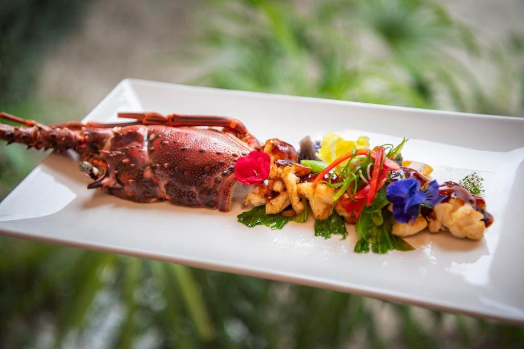 Gatavs ēdiens ar omāru, dekorēts ar krāsainām ziedu un dārzeņu garnējumiem, pasniegts uz baltas plāksnes.