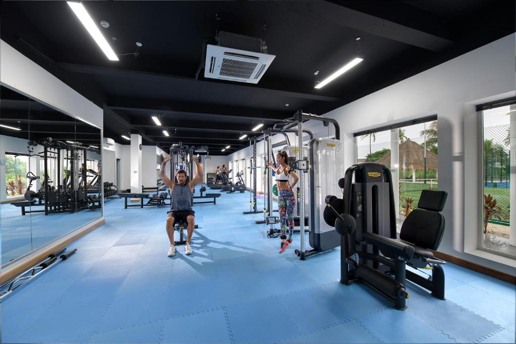 Moderns sporta zāles interjers ar trenažieriem, kur vīrietis veic vingrinājumus, bet blakus sieviete trenējas pie cita trenažiera. Gaismas un plašums rada motivējošu atmosfēru.