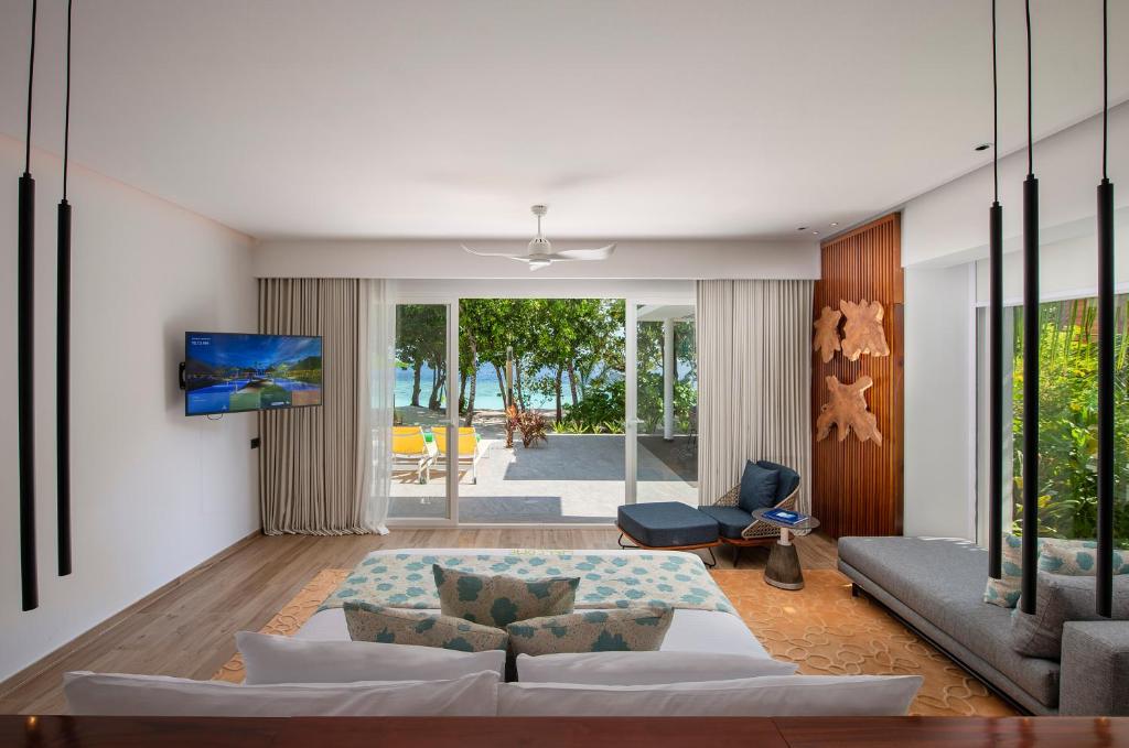 Mūsdienīgs viesistabas dizains ar skatu uz pludmali, kurā ir komfortabla dīvāna zona, televizors un liela stikla durvis, kas ved uz āra terasi.