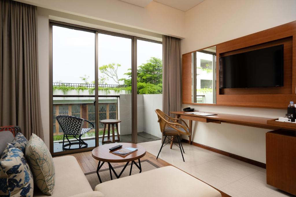 Mūsdienīgs viesnīcas numurs ar skatu uz dārzu, kurā ir komfortabla dīvāna zona, televizors un balkons. Interjers ir gaišs un elegants, ar koka un tekstila elementiem.