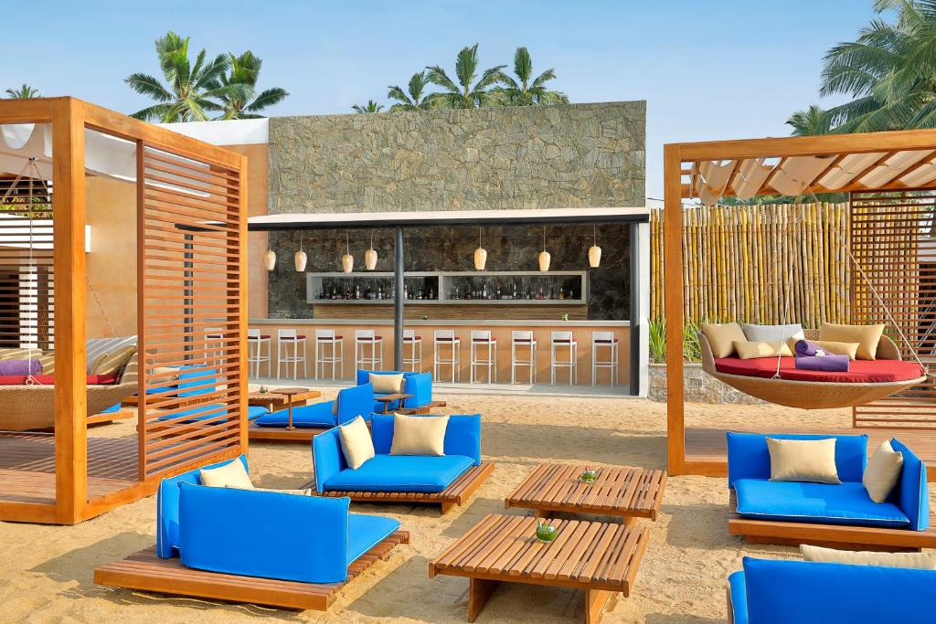 Pludmales bārs ar modernām mēbelēm, ziliem dīvāniem un koka galdiem, apkārt palmām un saulainam laikam. Ideāla vieta relaksācijai un atpūtai pie jūras.