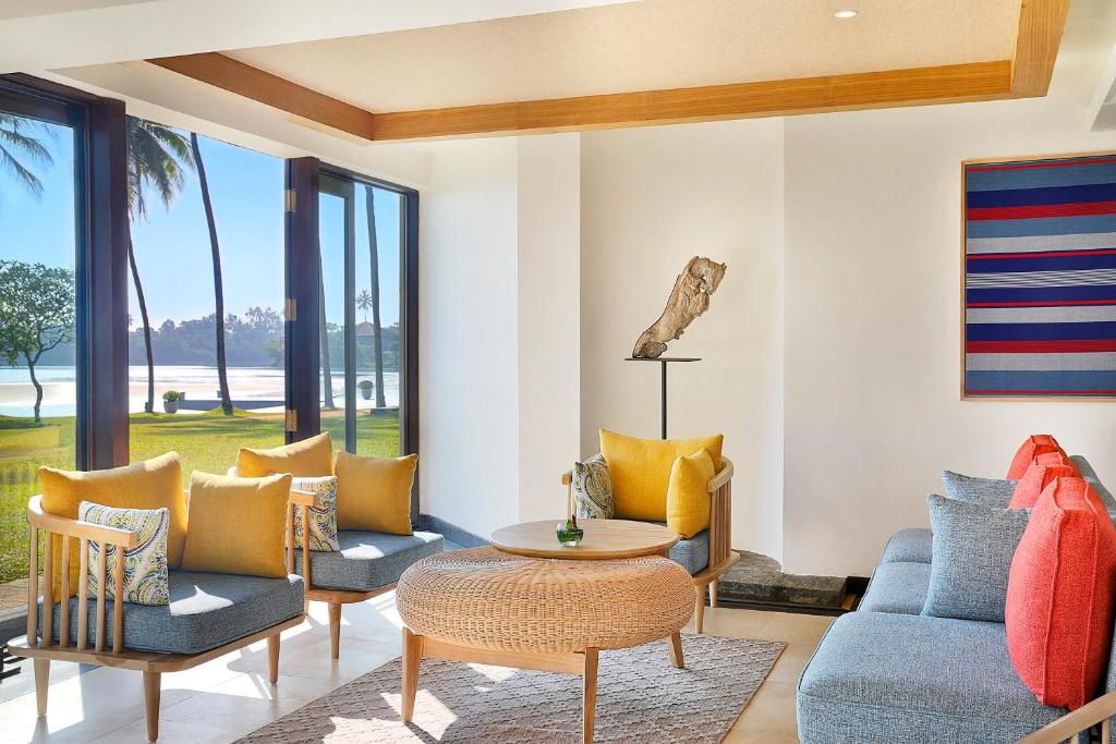 Mūsdienīgs un gaišs viesistabas interjers ar skatu uz dabu, kurā ir krāsaini dīvāni un ērtas krēsli. Lielie logi ļauj ieplūst dabiskajai gaismai un rada atvērtas telpas sajūtu.