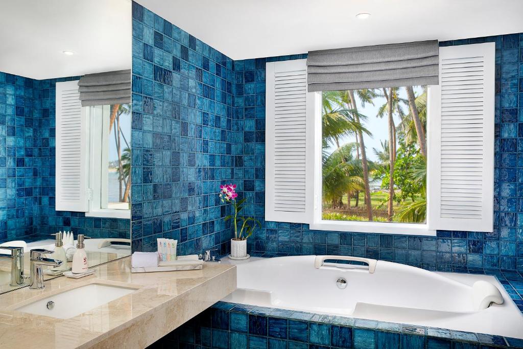 Mūsdienīga vannas istaba ar zilu mozaīkas apdari, baltu vannu un skatu uz palmu dārzu caur logu. Eleganta dizaina elementi piešķir telpai relaksējošu atmosfēru.