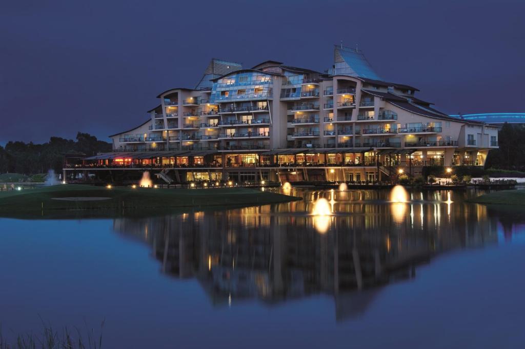 Sueno Hotels Golf Belek, elegants viesnīcas skats vakarā pie ūdens.