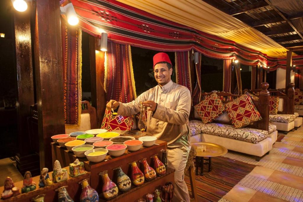 Vīrietis ar tradicionālo apģērbu, gatavojot krāsainus smilšu mākslas darbus Sunrise Arabian Beach Resort.
