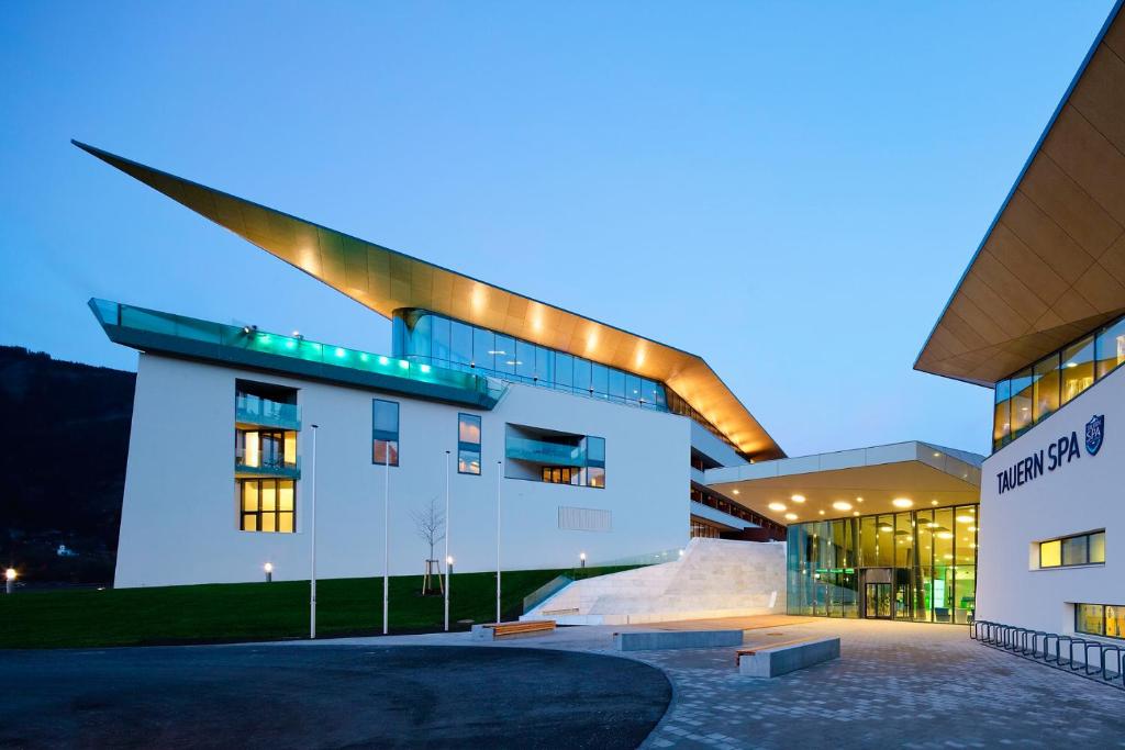 Mūsdienīga SPA ēka ar unikālu arhitektūru un izteiksmīgu jumta dizainu, apgaismota krēslā.