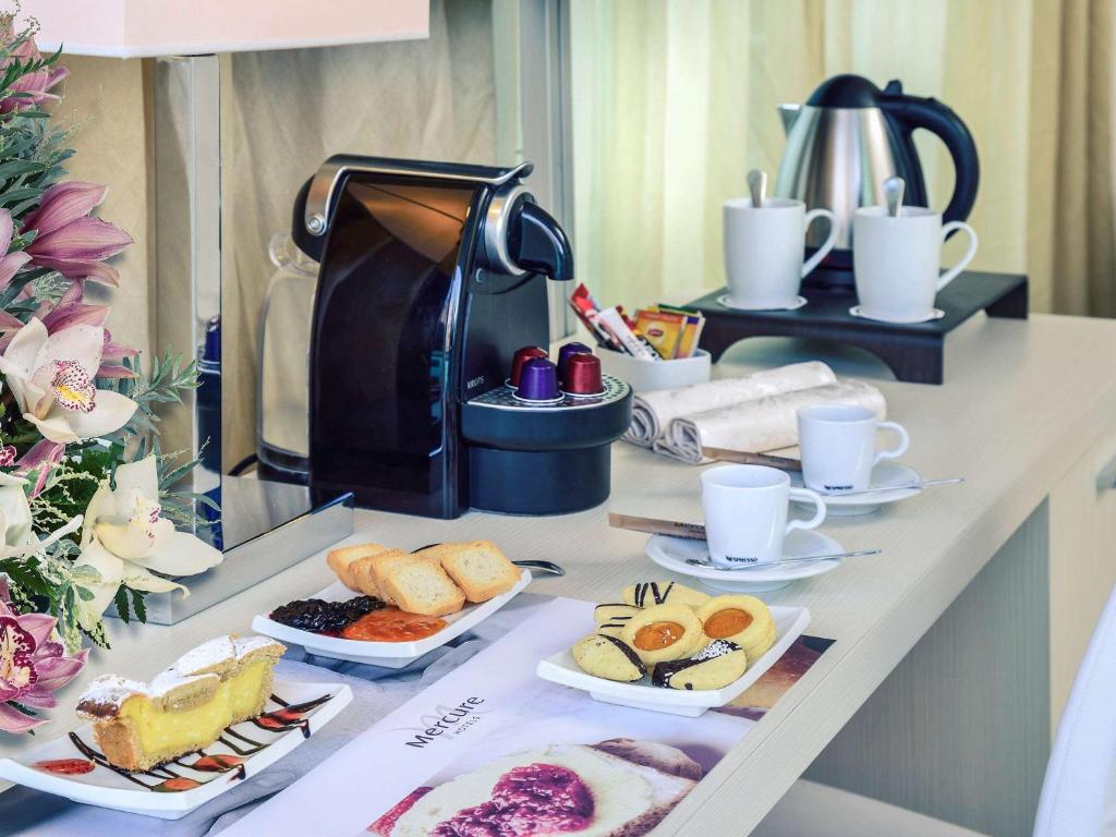 Broka, kas sastāv no kafijas, cepumiem un desertiem, izvietota uz galda blakus ziediem un kafijas automātam. Ideāla ainava relaksējošai brokastu pieredzei.