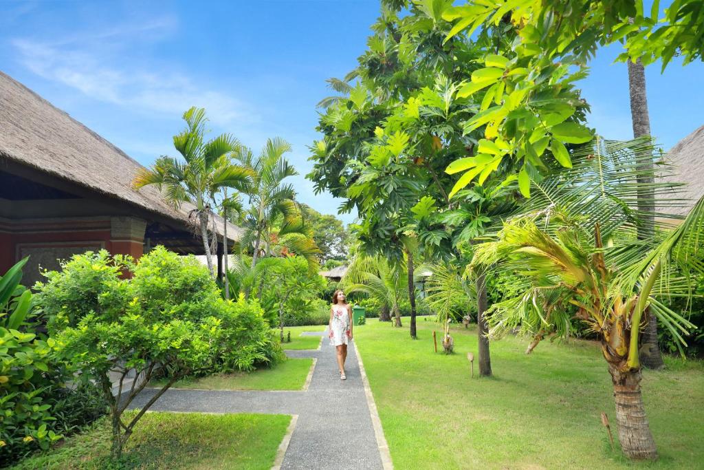 Skaistā dārza ainava pie viesnīcas Legian Beach ar pastaigājošu sievieti.