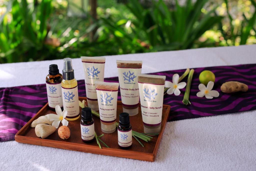 Dabīgās skaistumkopšanas produktu kolekcija, kas ietver ķermeņa skrubjus un eļļas, novietota uz koka tray ar ziediem un akmeņiem, radot relaksējošu atmosfēru spa vidē.