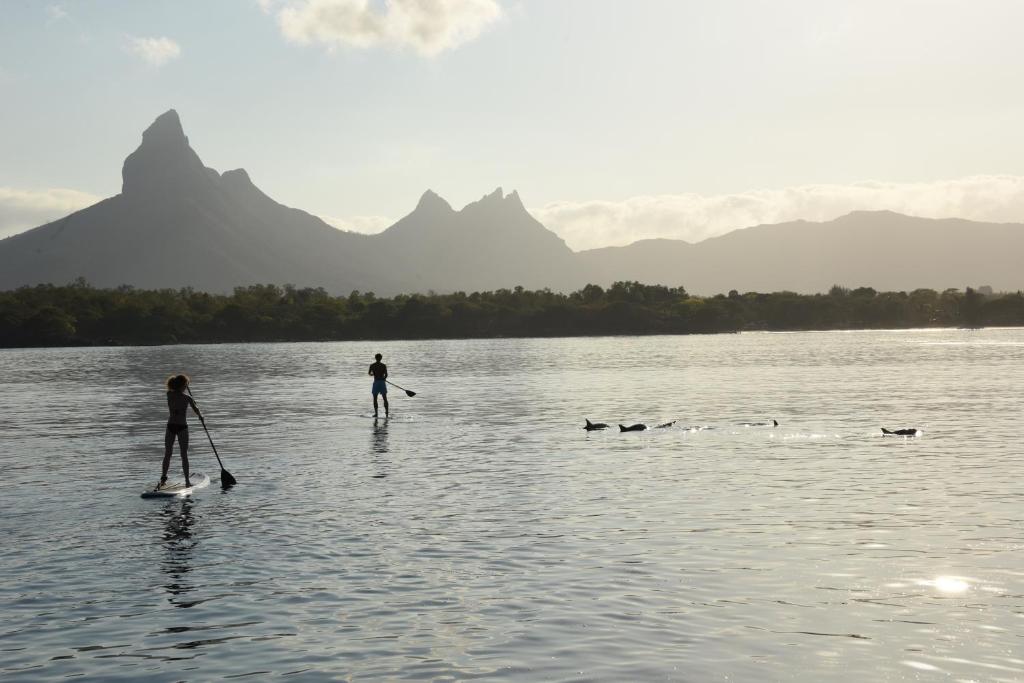 Divi cilvēki stāv uz SUP dēļiem pie Veranda Tamarin Hotel & Spa, fons kalni.
