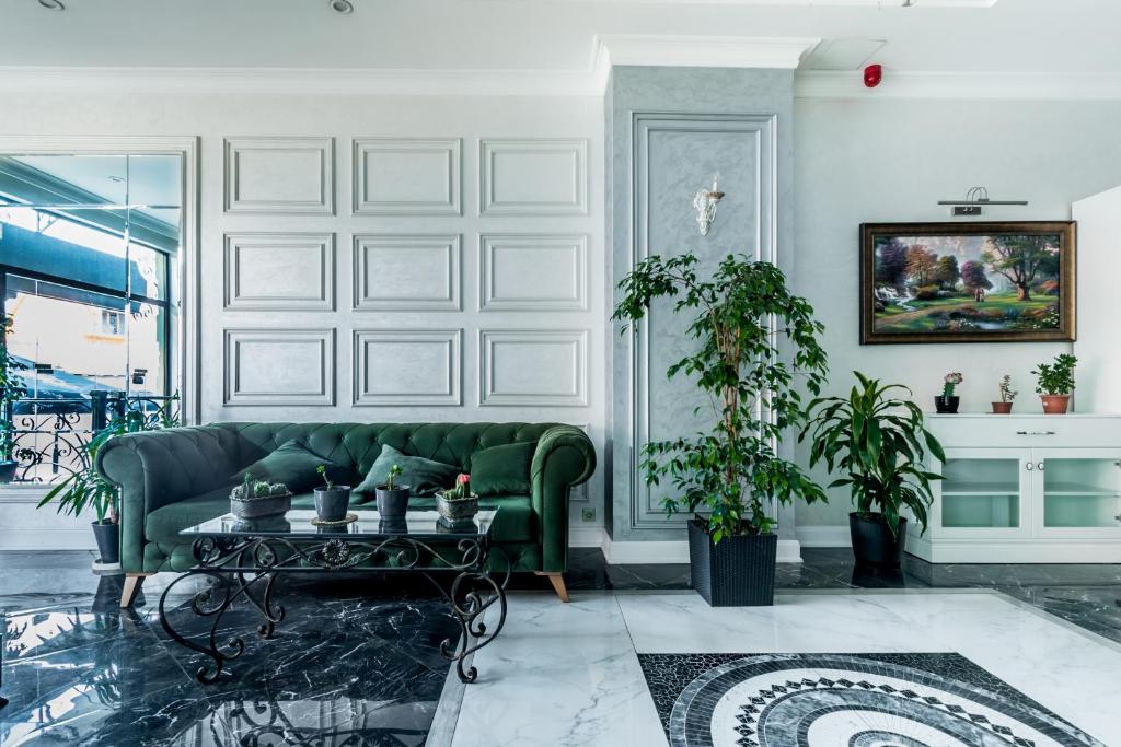 Elegants viesistabas interjers ar zaļu dīvānu, dekoratīviem augiem un mākslas darbiem uz sienas. Gaismas spēles un marmorētas grīdas radījušas modernu atmosfēru.