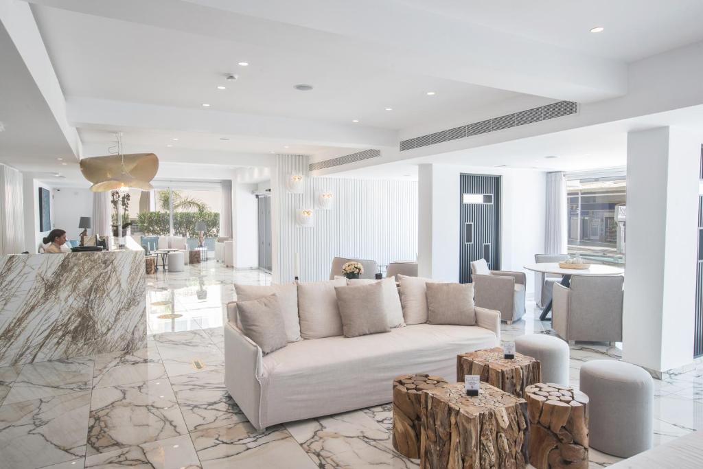 Mūsdienīgs viesnīcas vestibils ar elegantu dizainu, baltiem toņiem un marmora grīdu. Interjerā ir komfortablas dīvāns un koka galdi, radot relaksējošu atmosfēru.