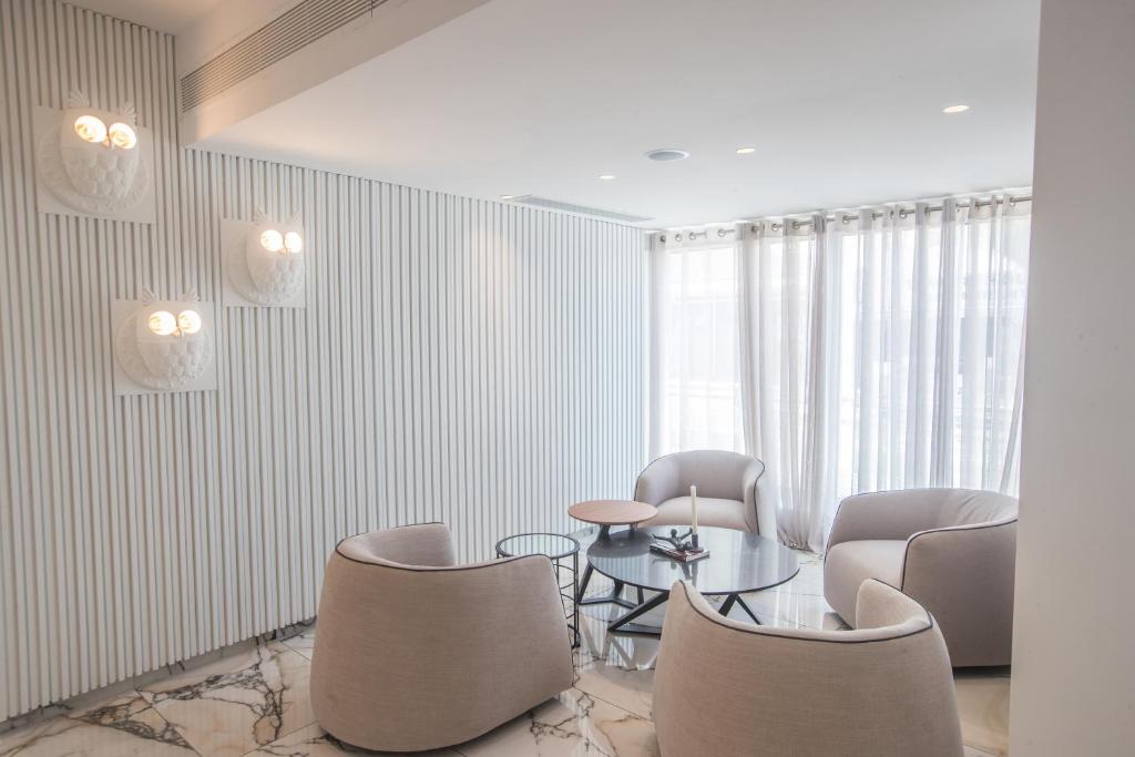 Moderns un minimālisks viesistabas interjers ar gaišām krāsām, noapaļotām mēbelēm un dekoratīvām sienu lampām. Telpā ir lieli logi ar caurspīdīgām aizkariem, radot mājīgu atmosfēru.