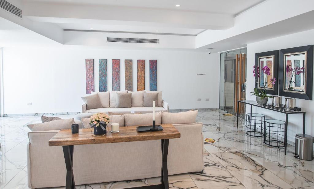 Mūsdienīgs viesistabas interjers ar gaišām sienām, elegantu dīvānu un koka galdu, uz kura atrodas ziedi un sveces. Sienas rotā krāsaini mākslas darbi, bet telpas apakšā ir marmora grīda.