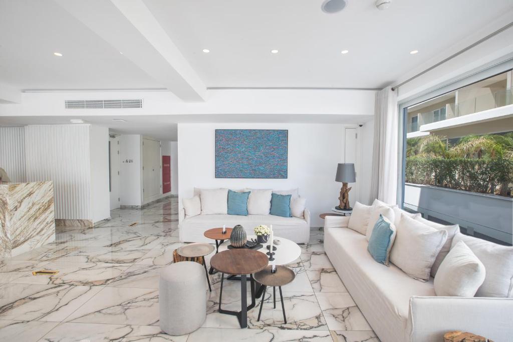 Mūsdienīga viesistaba ar marmora grīdu, gaišām mēbelēm un krāsainu mākslas darbu pie sienas. Telpā ir daudz gaismas un ērti sēdvietas.