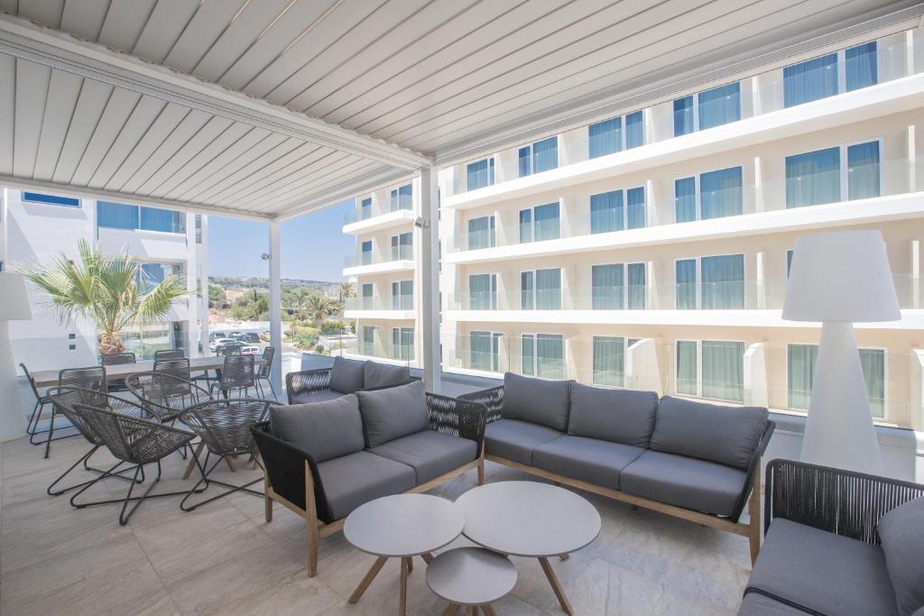 Mūsdienīgs terases dizains ar ērtām mēbelēm, kurā redzami dārza augi un viesnīcas ēka fona. Ideāla vieta relaksācijai un socializācijai.