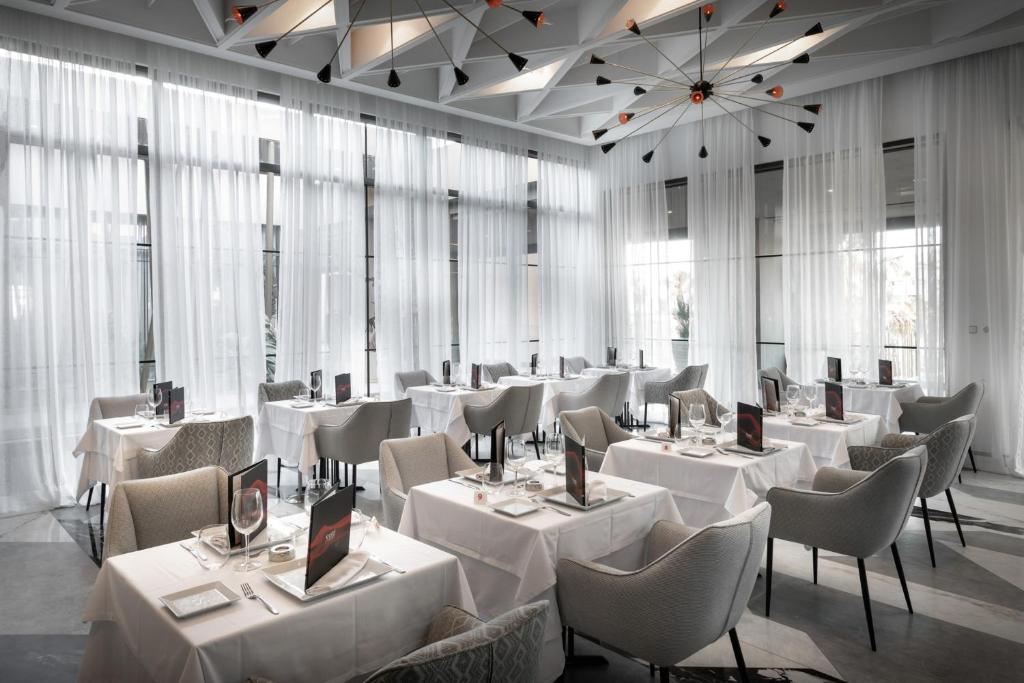 Elegants restorāns ar gaišām aizkariem, mūsdienīgu apgaismojumu un elegantām galdiņu iestatījumiem. Ideāla atmosfēra romantiskām un svinīgām vakariņām.